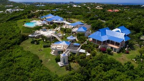 Luchtbeeld van een resort met meerdere gebouwen, een zwembad en weelderige begroeiing.
