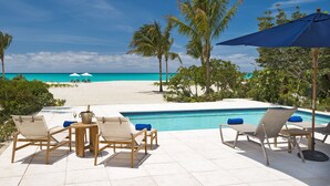 Un espace aménagé au bord de la piscine, avec des chaises longues, une petite table et une vue sur la plage et l’océan.
