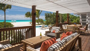 Un espace extérieur aménagé, abrité et doté de mobilier en osier, avec une piscine et une vue sur une plage et l’océan.