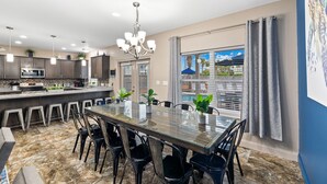 Een moderne keuken met donkere kastjes, een centraal keukenblok en een eethoek met een glazen tafel en stoelen.