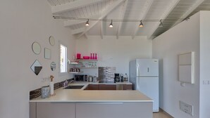 A modern kitchen with a central island, white cabinetry, and a high ceiling with exposed beams. - Villa Pinel – Intimate Oceanview Escape Above Orient Bay, St. Martin (Cul-de-Sac)