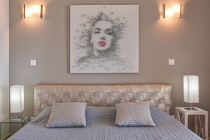 Une chambre à coucher avec une tête de lit capitonnée, deux lampes de chevet et une œuvre d’art accrochée au mur.