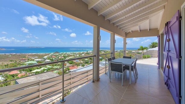 A balcony with a view of the ocean and a distant town. - Villa Pinel – Intimate Oceanview Escape Above Orient Bay, St. Martin (Cul-de-Sac)