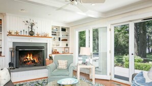 Un salón con chimenea, un sofá, una mesa de centro y vistas a través de puertas de cristal.