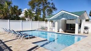 Une piscine avec des chaises longues, un espace de détente couvert et une clôture blanche.