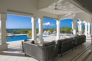A covered outdoor seating area with a pool view, white columns, and a ceiling fan. - Villa Océane – Elegant Ocean View Villa in Terres Basses, St. Martin (Terres Basses)