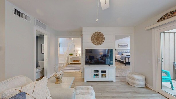A modern living room with a television, white furniture, and a view into the kitchen. - The Pool Is At Your Doorstep! (Hilton Head)