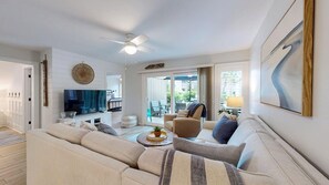 Ein Wohnzimmer mit einer Couch, Sesseln, einem Couchtisch, einem Fernseher und einem Deckenventilator.