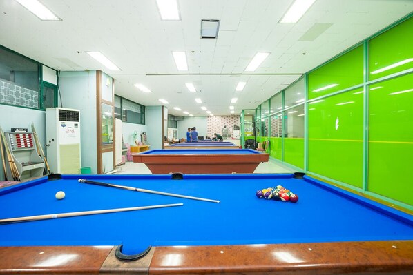 A pool table with balls and cues, a green wall, and a ceiling with lights.