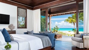 A modern bedroom with a large bed, a sofa, and a view of the beach. - Hawksbill Estate – A Grand Beachfront Estate on Grace Bay, Turks & Caicos (Leeward Settlement)