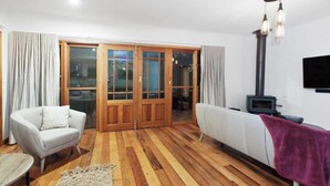 A living room with a wooden floor, a white sofa, a white armchair, a small table, a fireplace, and a TV mounted on the wall. - 5 Connelly - Echuca Holiday Homes (Echuca)
