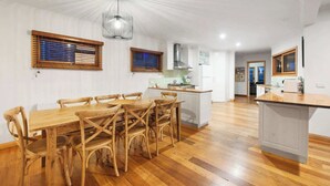 A spacious kitchen with a wooden dining table and chairs, a central island, and a modern pendant light. - 5 Connelly - Echuca Holiday Homes (Echuca)