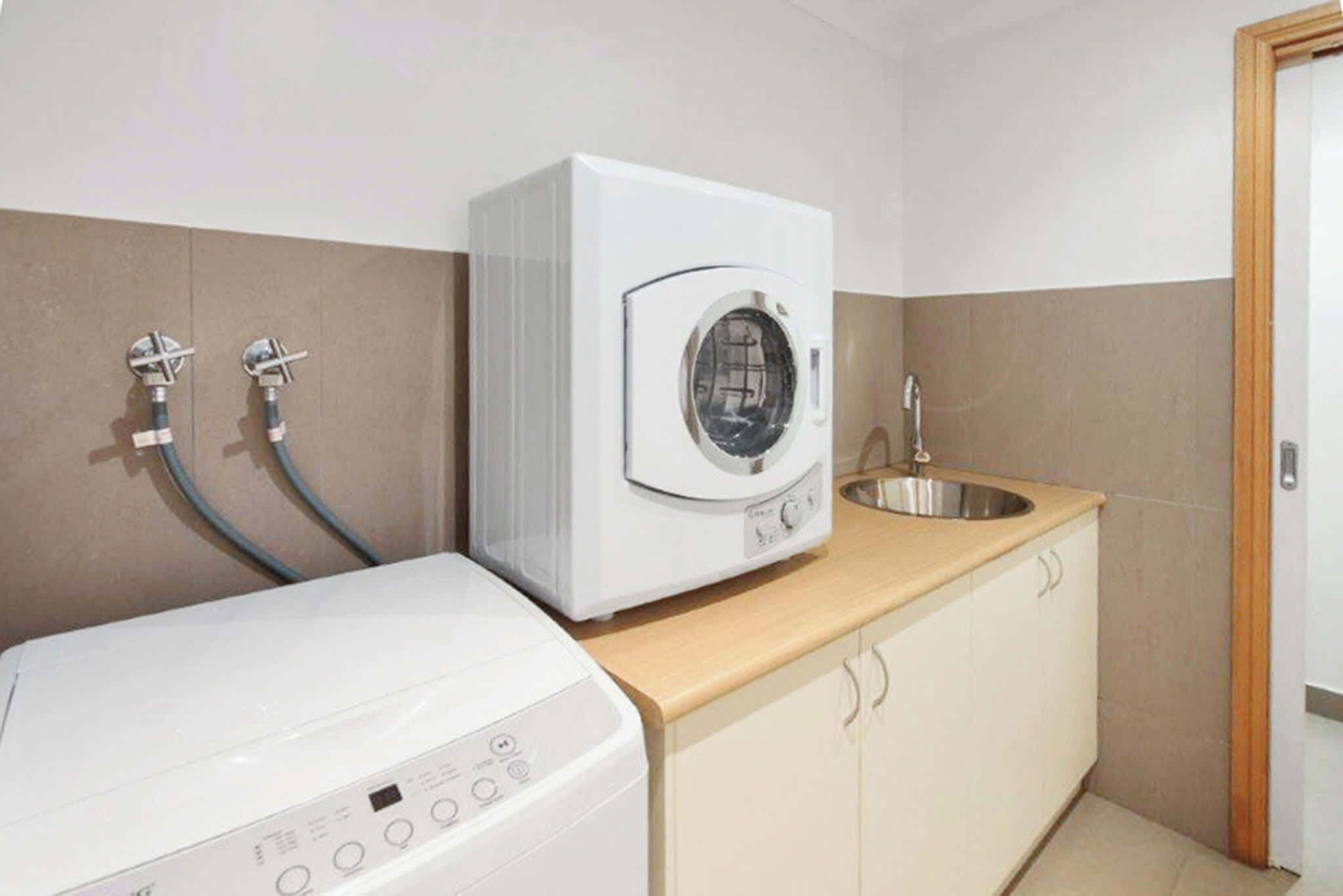A laundry area with a washing machine and a dryer, a sink, and a wooden countertop.