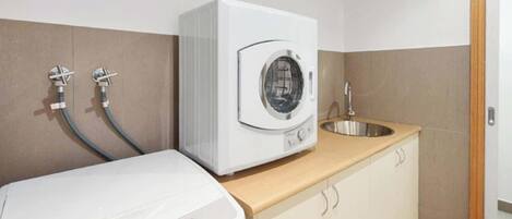 A laundry area with a washing machine and a dryer, a sink, and a wooden countertop.