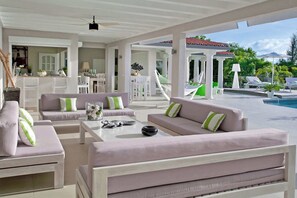 Un vaste espace de vie extérieur avec une piscine, des meubles blancs et une vue sur la piscine et la verdure.