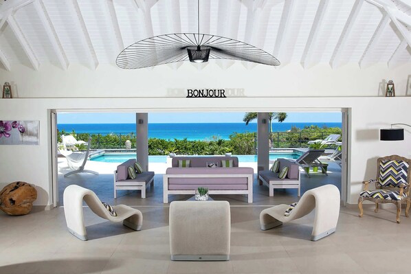 Un salon moderne avec vue sur l’océan, un ventilateur de plafond et un panneau indiquant « BONJOUR ».