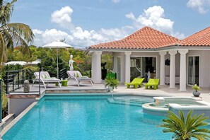 Une piscine avec des chaises longues, une statue et un bâtiment doté d’un toit en tuiles.