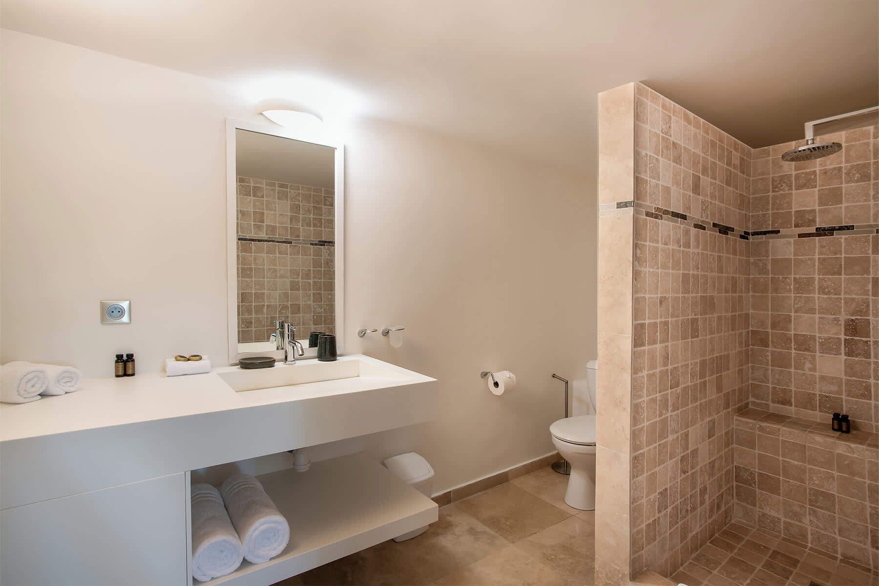Un bagno moderno con un mobile lavabo bianco, un ampio specchio, una doccia con piastrelle color crema e un water.