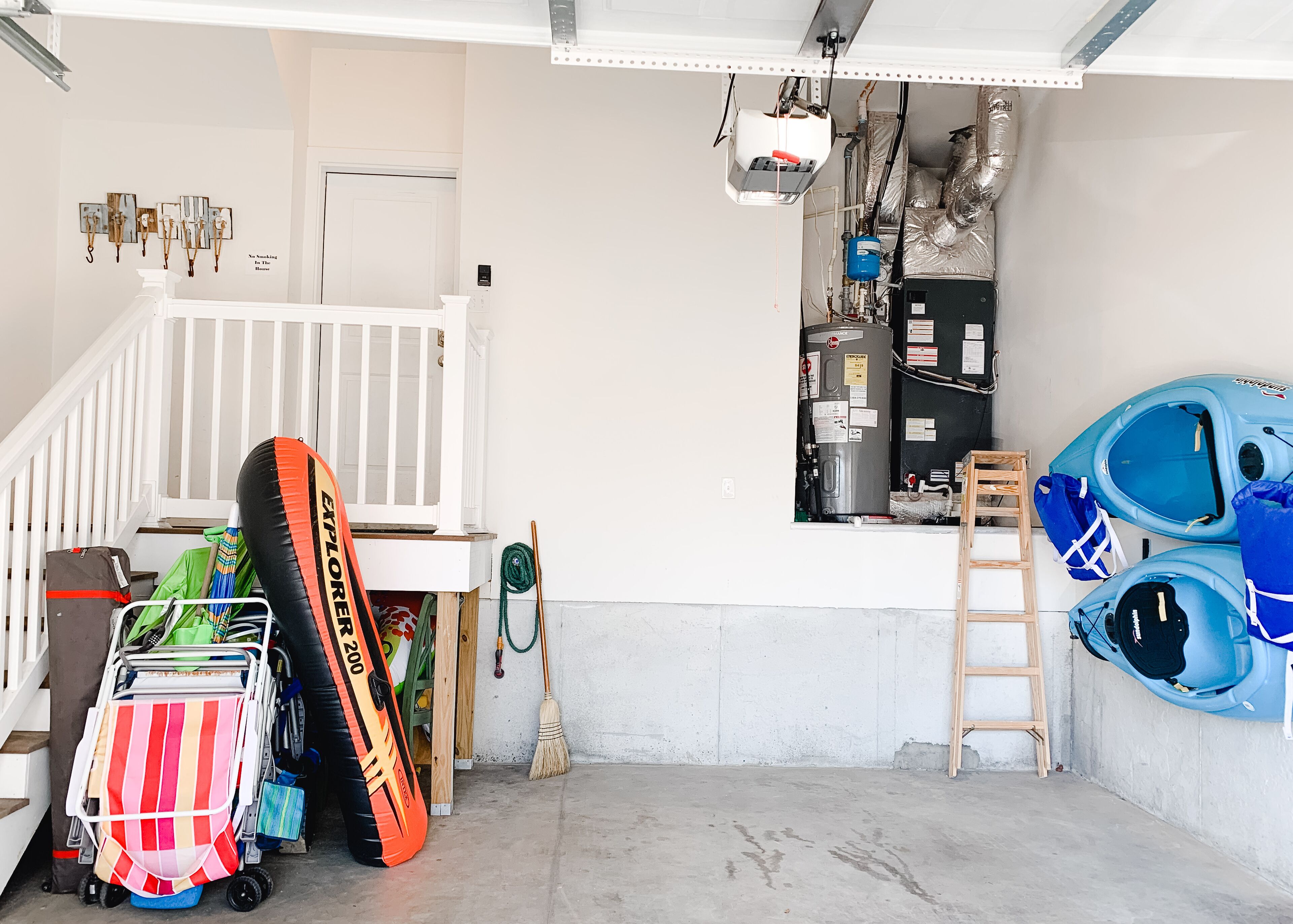 Eine Garage mit weißer Treppe, einem weißen Babybett, einem großen Warmwasserspeicher, Kajaks und einem Wagen mit einer Streifen tasche.