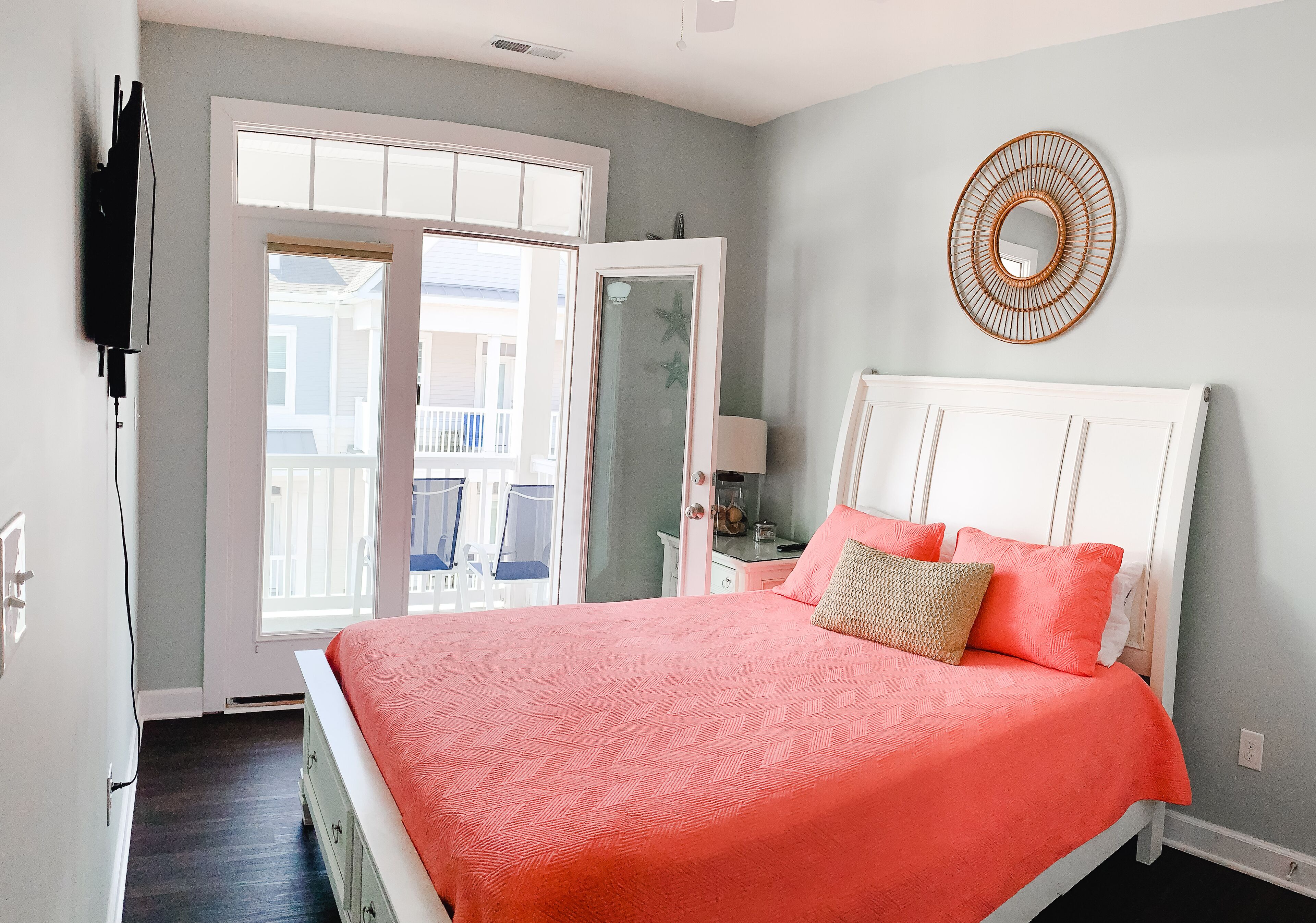 Une chambre à coucher avec un lit, une tête de lit blanche, un élément de décoration circulaire sur le mur et une fenêtre donnant sur un balcon.