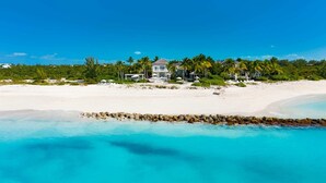 Een pand aan het strand met een groot huis, palmbomen en een zandstrand.