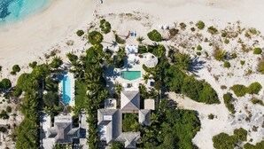 Luchtbeeld van een strandpand met zwembad, meerdere gebouwen en weelderige begroeiing.
