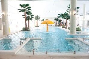 Una piscina interior con múltiples fuentes, palmeras y una fuente central.