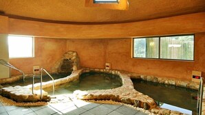 Een wellnessruimte met een stenen hottub, betegelde vloer en een klein raam.