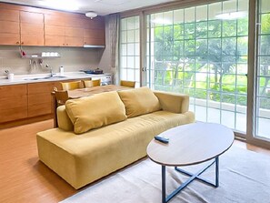 A modern living room with a sofa and a small table, wooden cabinets, and a large window with a view of greenery. - GoChang Well Park City Healing County (Gochang)