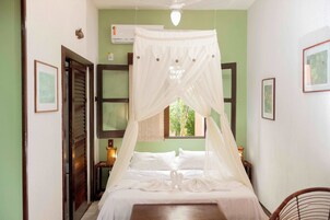 Un dormitorio con una cama bajo un dosel, una mesita de noche con lámpara y una ventana con vistas al verdor.
