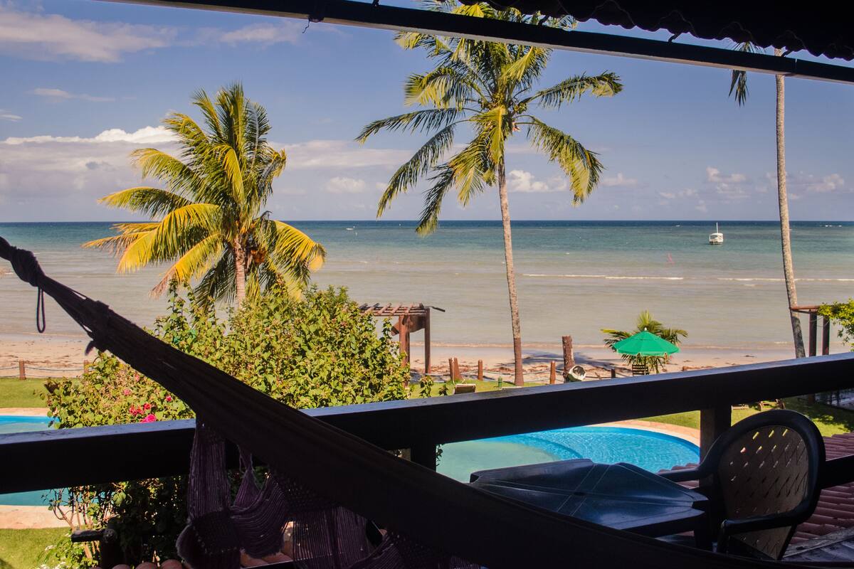 Una hamaca, una piscina y vistas a la playa con palmeras.