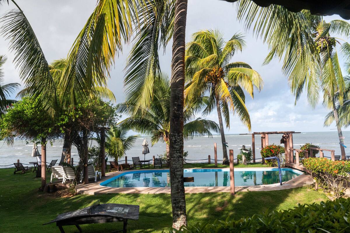 Zona de piscina con palmeras y vista al océano.
