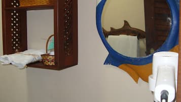 A bathroom with a wooden shelf holding a basket and a towel, a round mirror with a fish design, and a hairdryer plugged in.