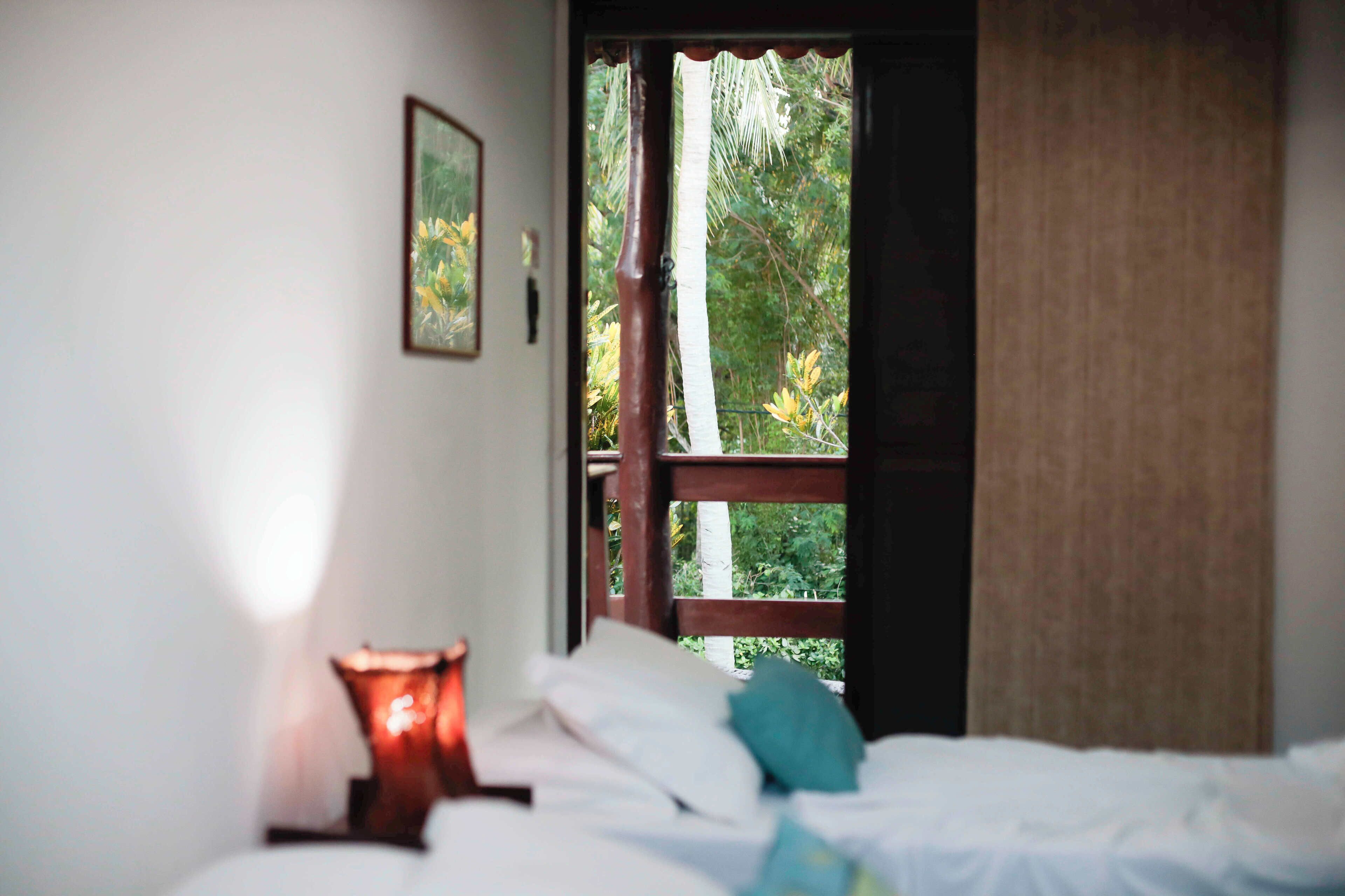 Un dormitorio con cama, mesita de noche, lámpara y ventana con vistas a árboles.