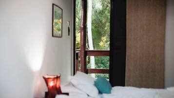 Un dormitorio con cama, mesita de noche, lámpara y ventana con vistas a árboles.