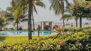 A pool area with a pergola, palm trees, and a view of the beach.