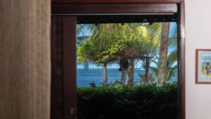 A view through a doorway to a balcony with a palm tree and ocean in the background.