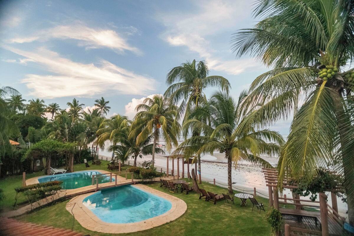 Piscina rodeada de palmeras y vista a la playa.
