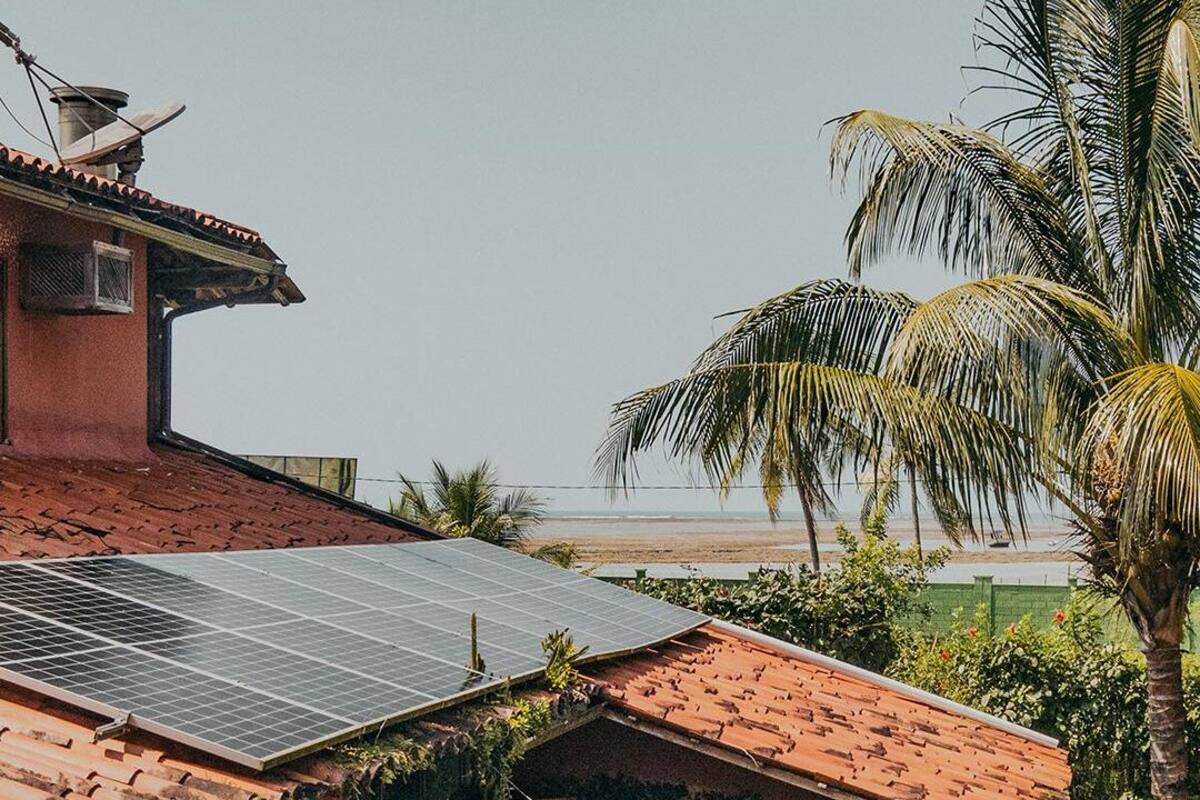 Una casa con panel solar en el techo, estructura de techo de paja y vista a la playa.