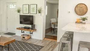 A modern living room with a flat-screen TV, a fireplace, and a dining area with stools. - The Sycamore Bungalow located near attractions in The Amish Country.  (Lancaster)