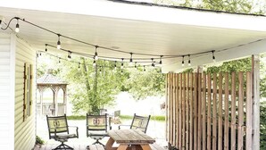 A covered patio with a wooden table and chairs, a string of lights, and a wooden fence. - The Sycamore Bungalow located near attractions in The Amish Country.  (Lancaster)