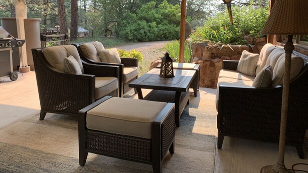 An outdoor patio with wicker furniture, a grill, and a view of the surrounding forest. - Historic 1925 Pine Cone Inn (Sandia Park)