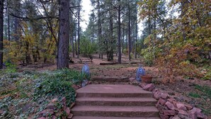 A set of stone steps leading into a forested area with picnic tables and decorative lanterns. - Historic 1925 Pine Cone Inn (Sandia Park)