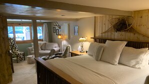 A cozy bedroom with a large bed, wooden headboard, and a view of the outdoors. - Historic 1925 Pine Cone Inn (Sandia Park)