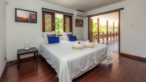 Ein Schlafzimmer mit einem großen Bett, Holzboden und Blick auf einen Garten durch eine offene Tür.