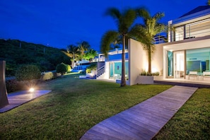 A modern house with a well-maintained lawn, a wooden deck, and a staircase leading to a second floor.