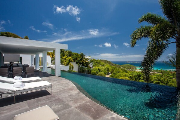 A modern infinity pool with a clear view of the ocean and a lush green landscape.