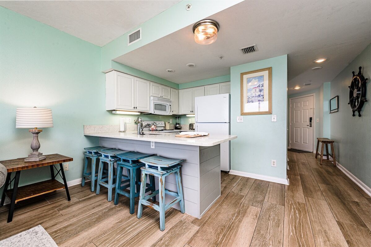 A kitchen with a central island, bar stools, a microwave, and a refrigerator.
