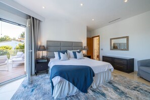 A modern bedroom with a large bed, a nightstand, a dresser, and a mirror. - Villa Verde Subach by Balearic Villas (Pollensa)