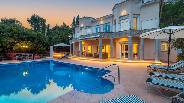 Una casa de dos pisos con piscina, mobiliario exterior y un patio cubierto.